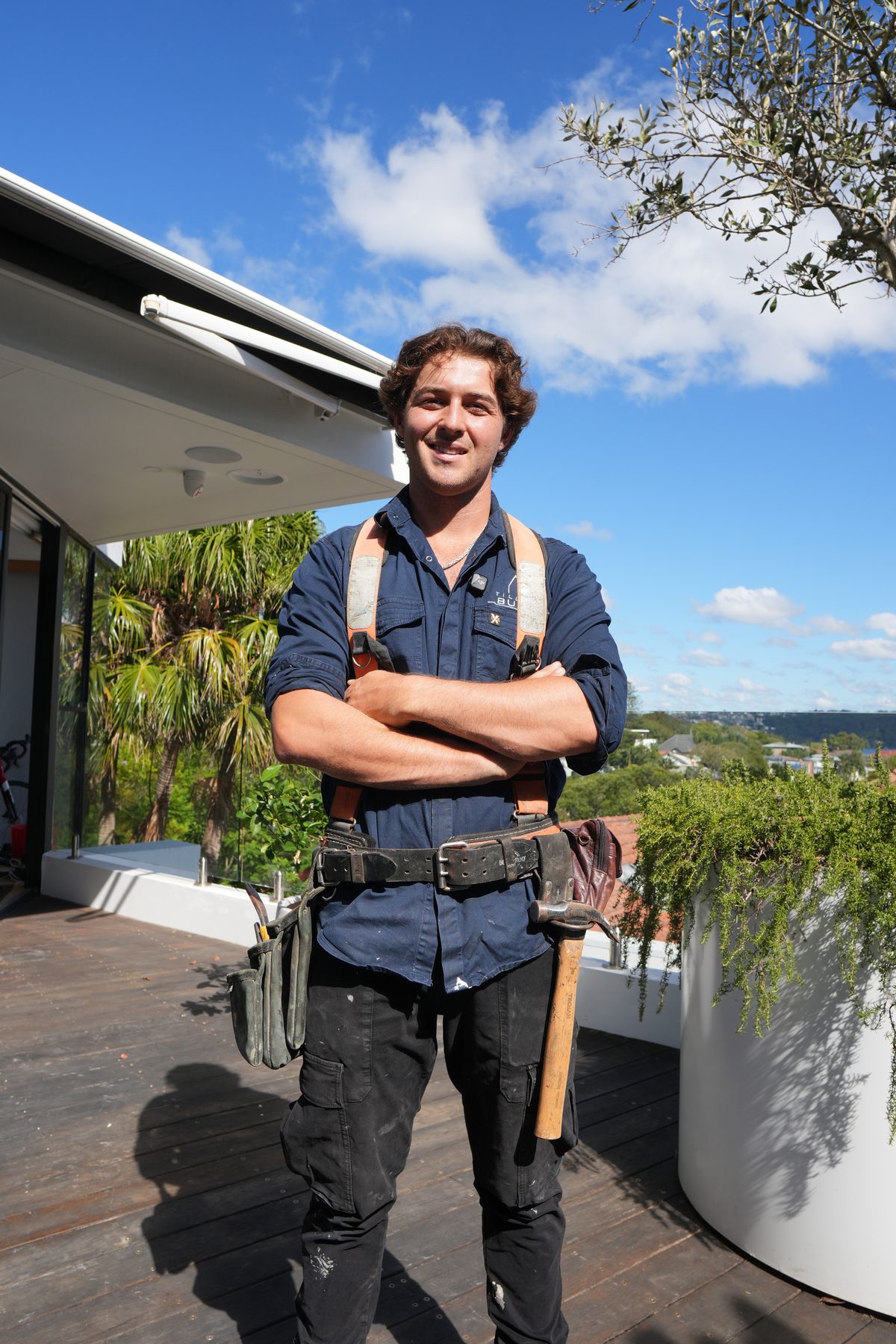 Hubert Auld — owner-operator of Tillow Built — on a Sydney rooftop deck with tool belt
