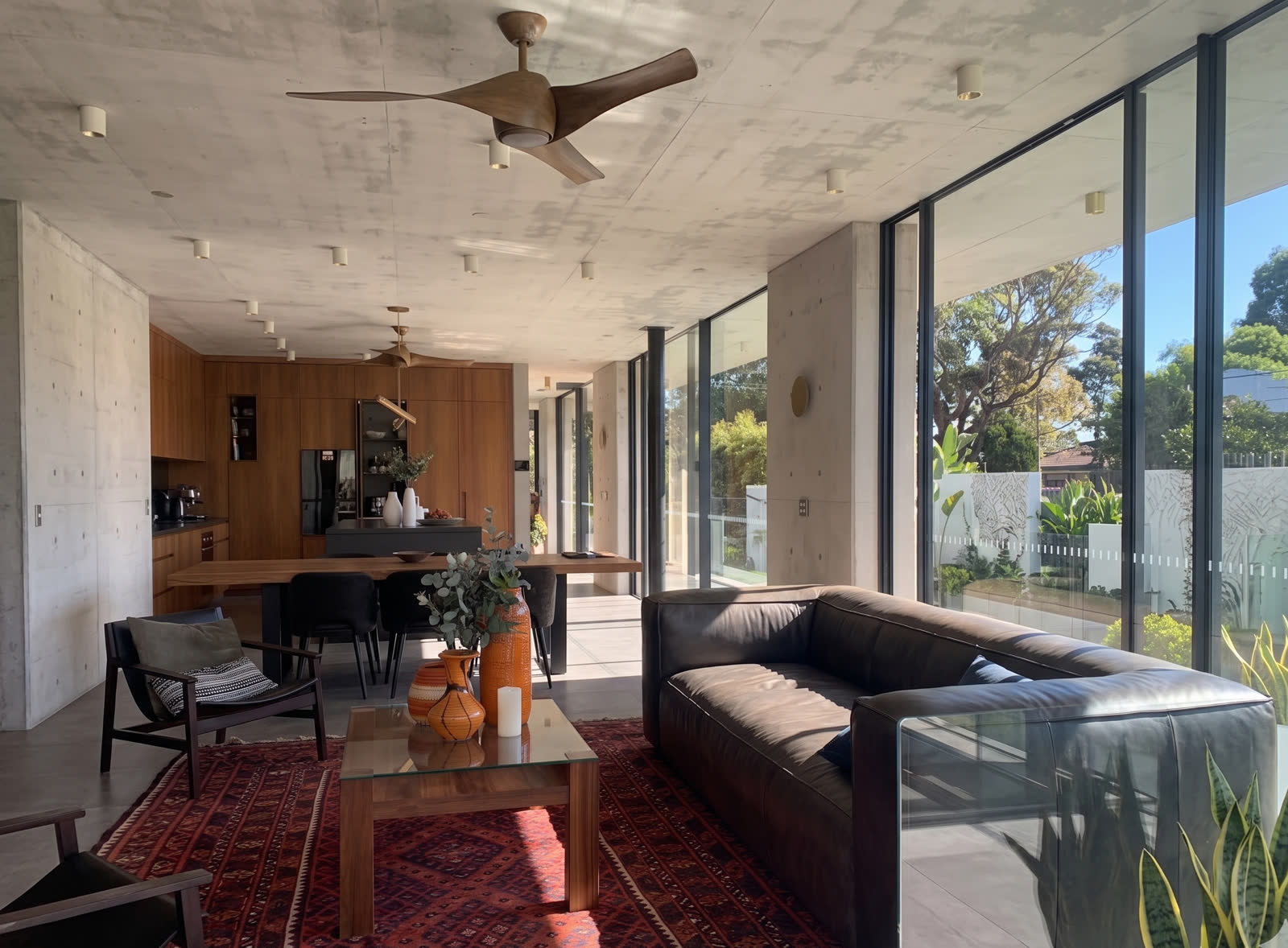 Living room with leather sofa, timber-lined kitchen and off-form concrete ceiling opening to the garden, Bronte award house